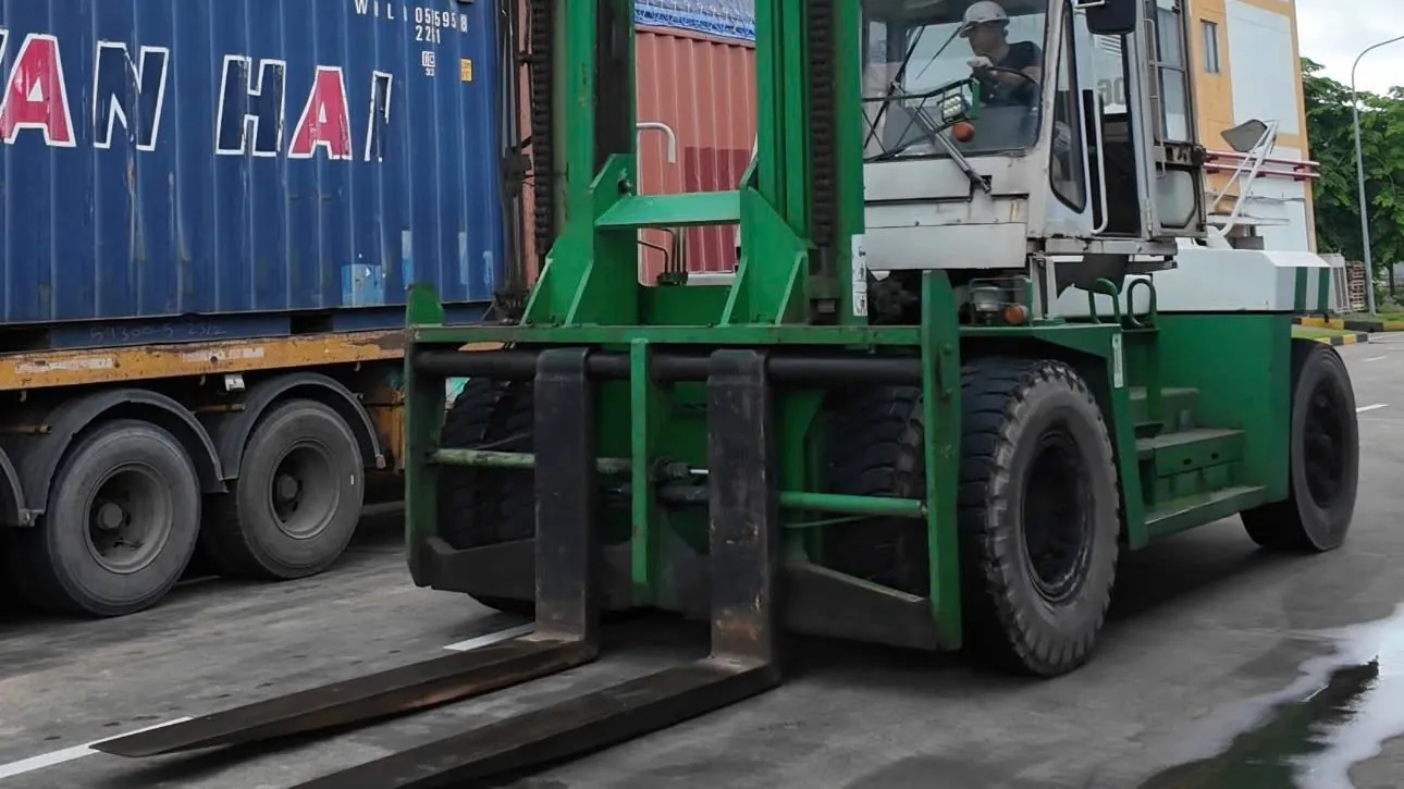 Xe nâng hạng nặng xanh trắng cạnh container tại nhà máy